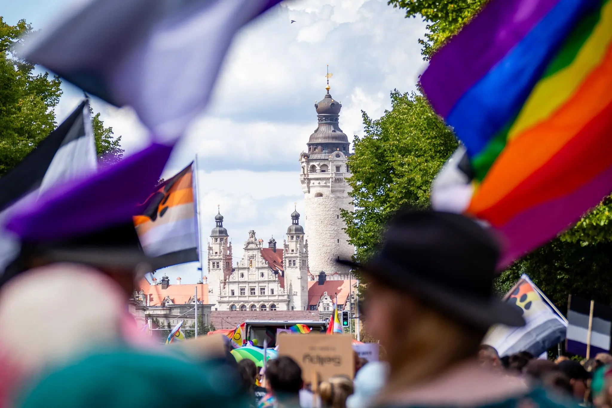 Menschenmenge mit verschiedenen Pride-Flaggen und Ausblick auf das neue Rathaus in Leipzig